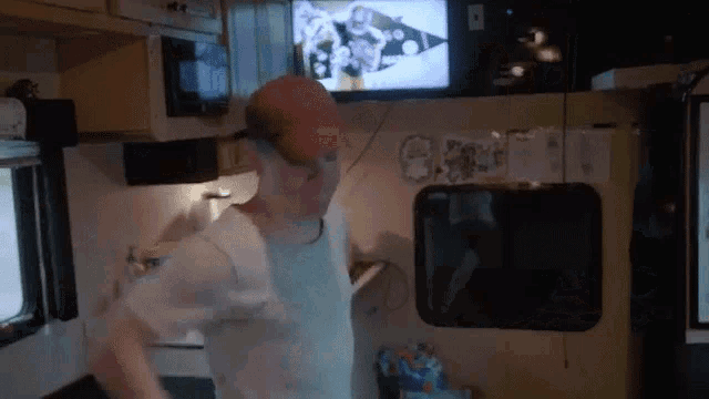 a man in a red hat is dancing in a kitchen while watching a television .