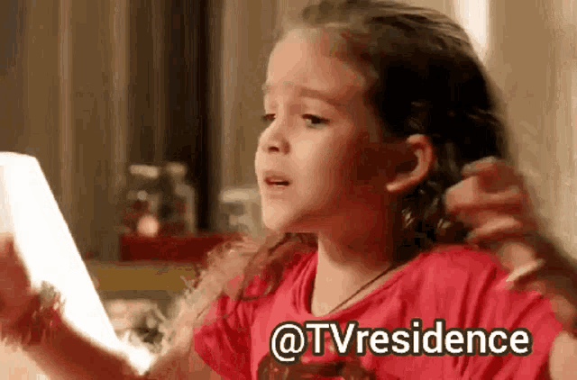 a little girl in a red shirt is looking at herself in a mirror with the words @tvresidence below her