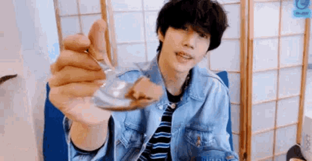 a young man in a denim jacket is holding a glass spoon .
