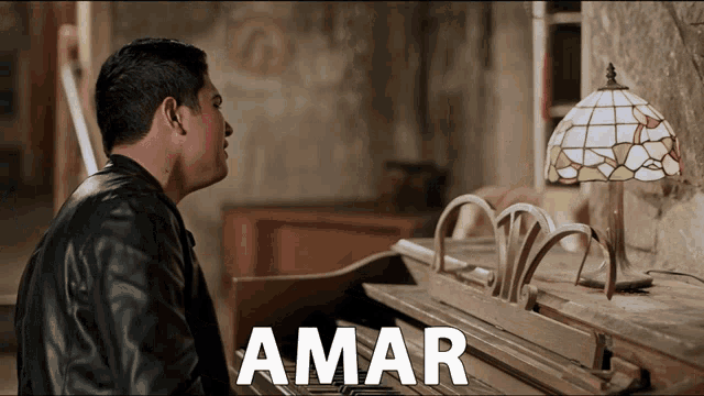 a man sits at a piano with the word amar written above him