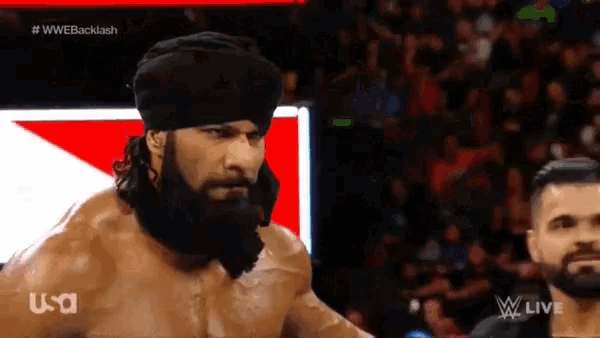 a man with a beard is standing in front of a screen that says wwe backlash