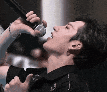 a close up of a person singing into a microphone with the letter t on his shirt