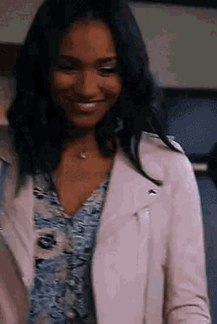 a woman is wearing a pink leather jacket and a floral shirt and smiling .