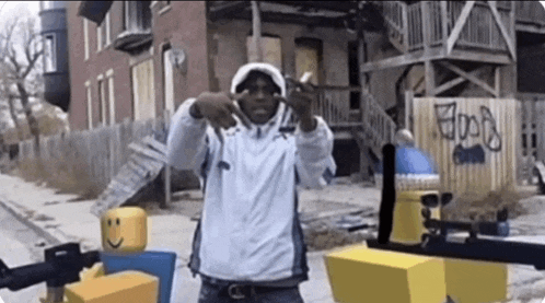 a man in a white hoodie is standing in front of a building with graffiti on it that says hood