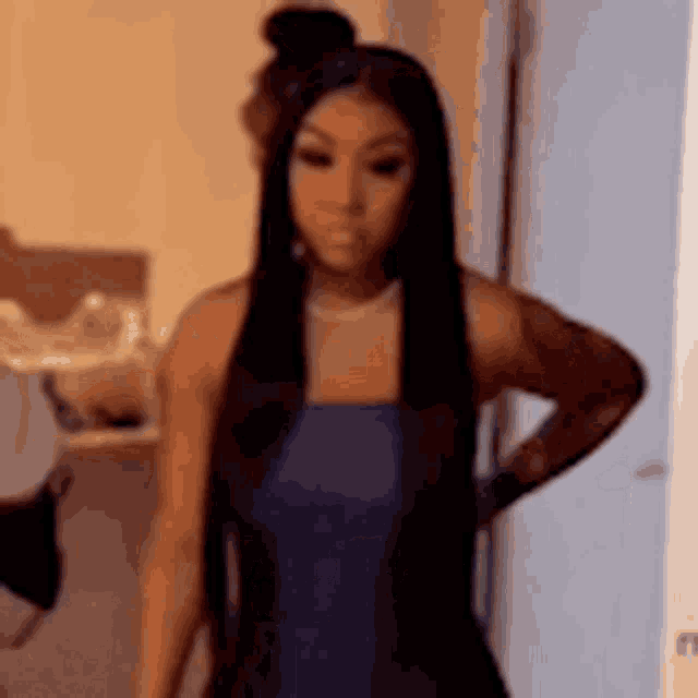 a woman with long black hair is standing in a room with her hands on her hips and looking at the camera .