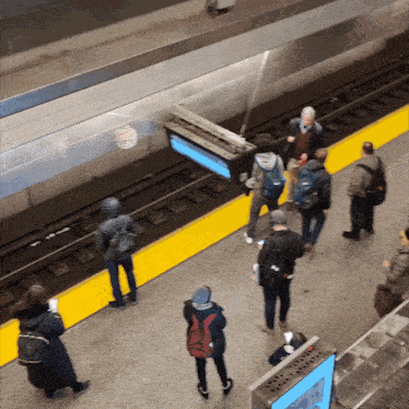 a group of people standing on a train platform with a sign that says ' subway ' on it