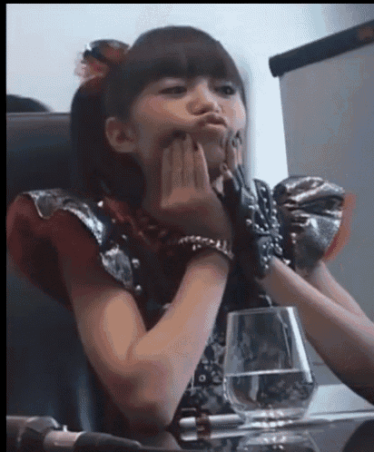 a girl is sitting at a table with a glass of water and making a face .