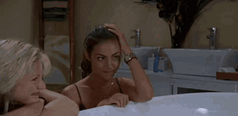 two women are sitting in a bathtub looking at a mirror .