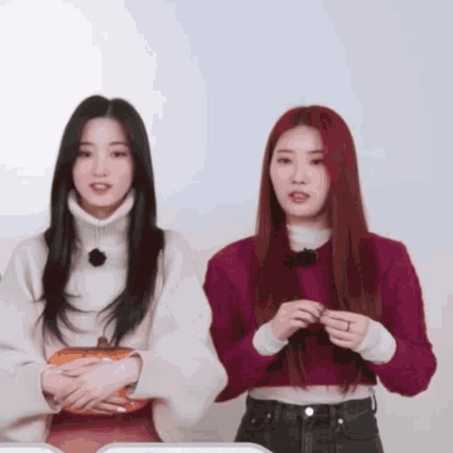 two women standing next to each other with one wearing a white turtleneck