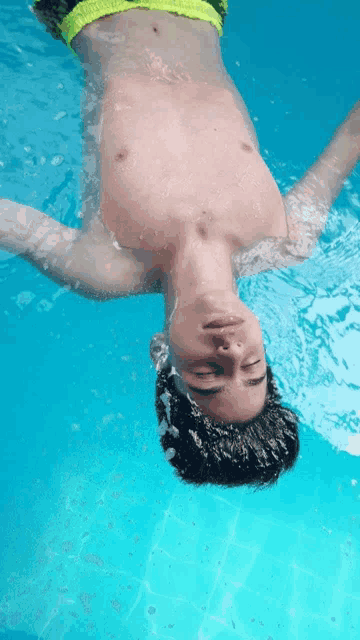 a boy is floating upside down in a pool