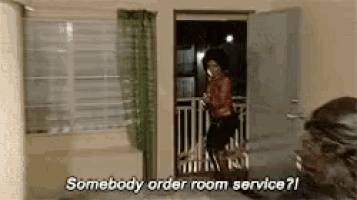 a woman is standing in a room talking on a cell phone and asking someone to order room service .