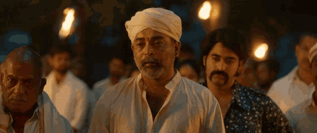 a man with a beard wearing a white turban stands in a crowd of people