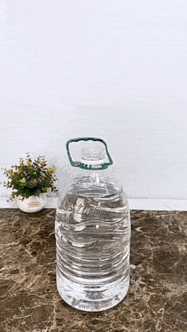 a bottle of water with a green handle is sitting on a marble counter top next to a potted plant .