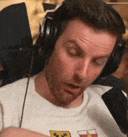 a man wearing headphones and a white shirt with a flag on it is looking down