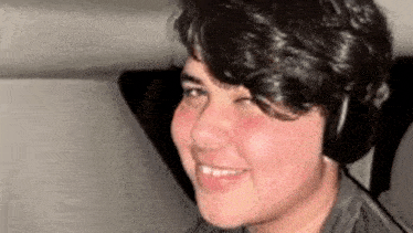 a young man wearing headphones is smiling while looking at the camera .