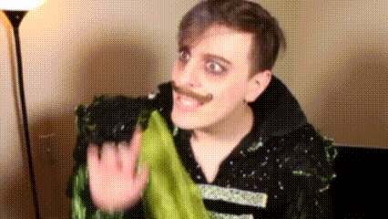 a man with a mustache is waving at the camera while wearing a black and green costume .