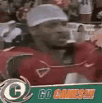 a man wearing a baseball cap and a red jersey is standing in front of a sign that says `` go games '' .