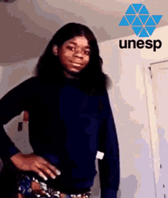 a woman in a blue sweater stands with her hands on her hips in front of a unesp logo