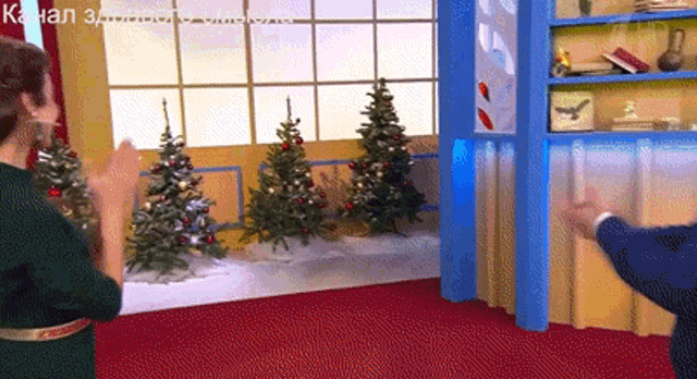 a man and woman are clapping in front of christmas trees on a set