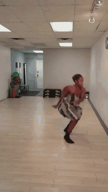 a woman in a dress is dancing in a hallway with an exit sign above her