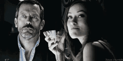 a man and a woman are standing next to each other . the man is holding a martini glass .