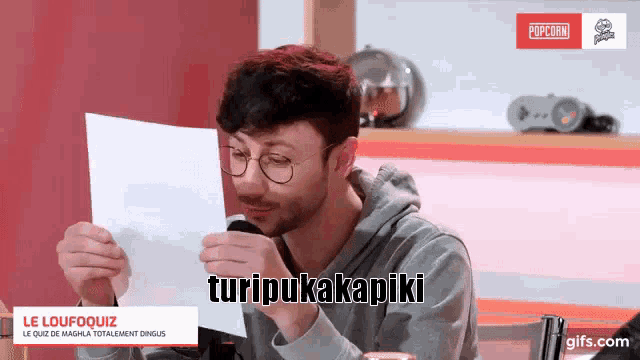a man with glasses is holding a piece of paper that says turipukakapiki on it