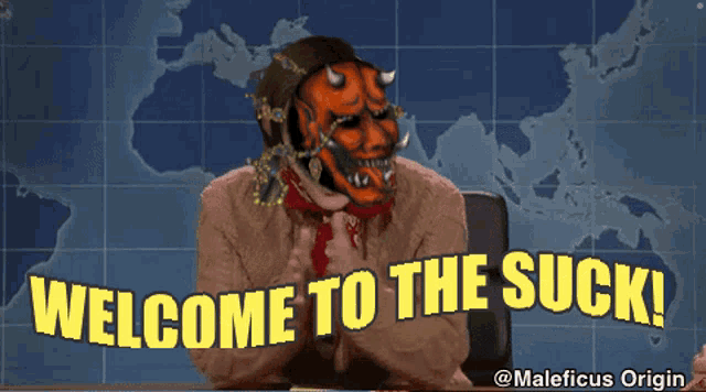 a man wearing a mask says welcome to the suck while sitting at a desk