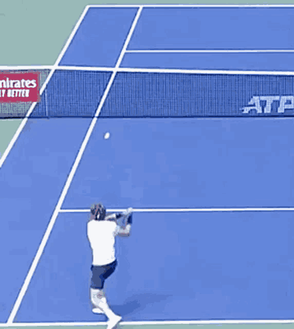 a man is playing tennis on a blue court with an emirates ad behind him