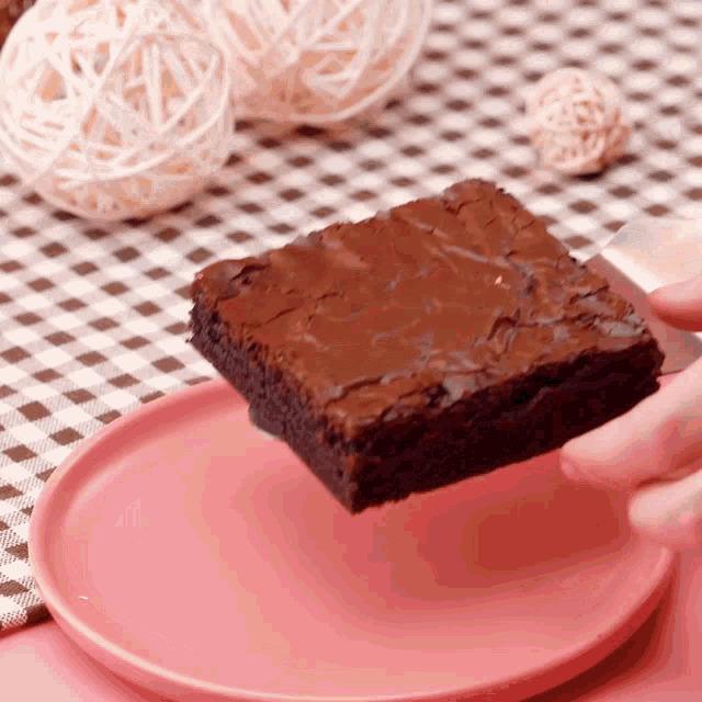 a person holds a piece of brownie on a pink plate