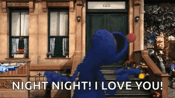 elmo from sesame street is standing in front of a building holding a red heart .