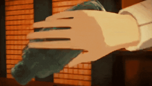 a hand is holding a blue object in front of a brick wall ..
