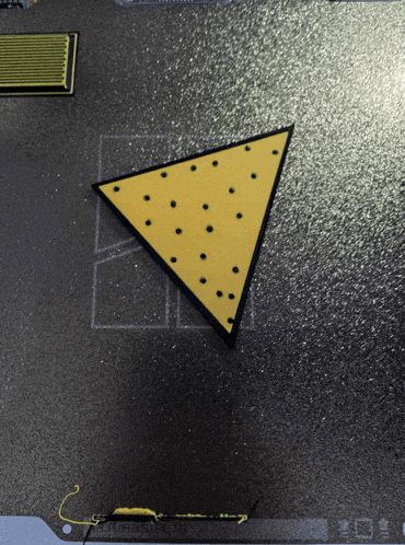 a yellow triangle with black dots on it is on a black surface