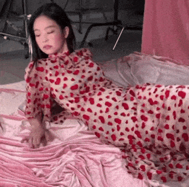 a woman is laying on a bed wearing a red and white polka dot dress .
