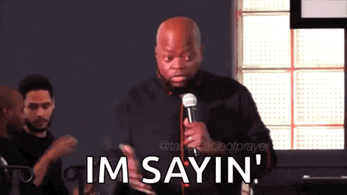 a man speaking into a microphone with the words im sayin behind him