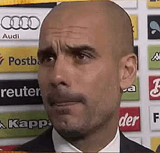 a bald man with a beard is making a funny face in front of a wall with advertisements for audi and kappa