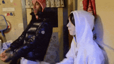 a man in a black jacket and a woman in a white hoodie are standing next to each other in a room