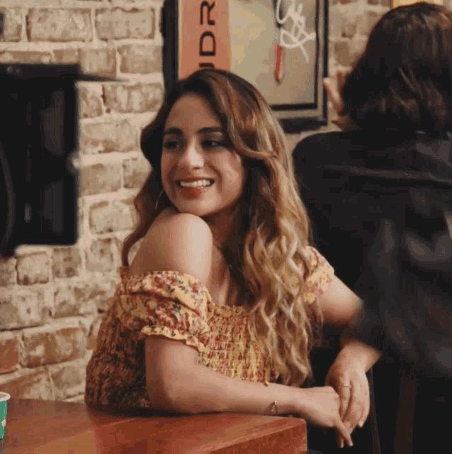 a woman sits at a table in front of a brick wall and a sign that says ' rider ' on it