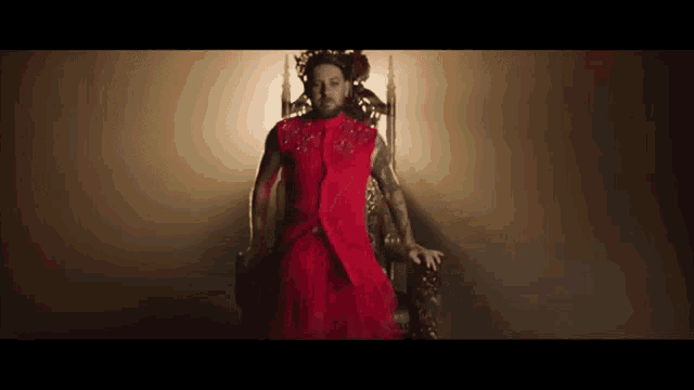 a man wearing a red dress is sitting on a throne