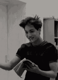 a young man is smoking a cigarette while holding a book and a cell phone .