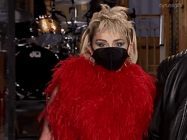 a woman wearing a red fur coat and a black mask is giving a thumbs up sign .
