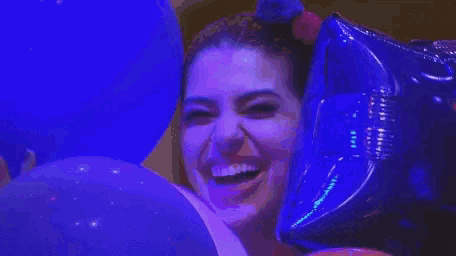a woman is holding a blue balloon and smiling while surrounded by blue balloons .