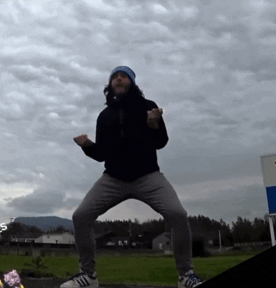 a man in a black jacket and gray pants is dancing in front of a cloudy sky