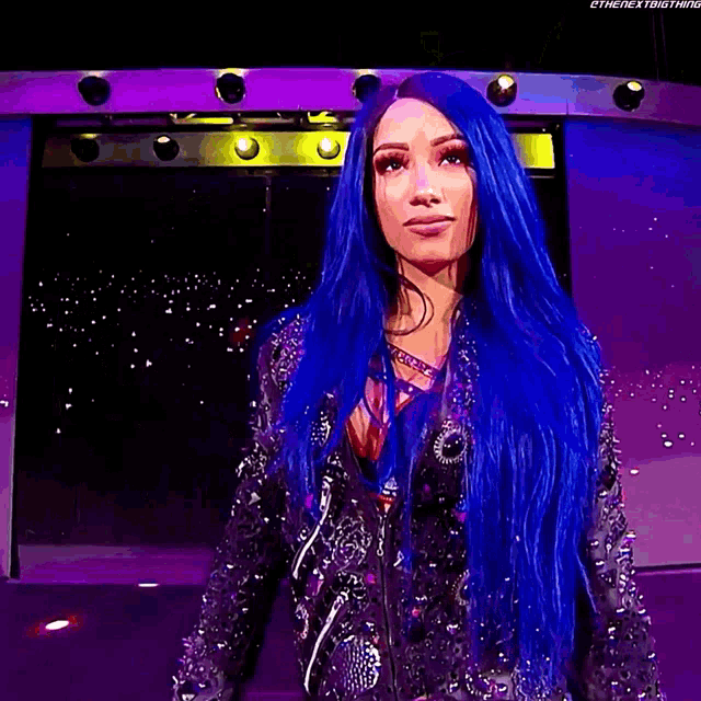 a woman with blue hair is wearing a black jacket with spikes on it .