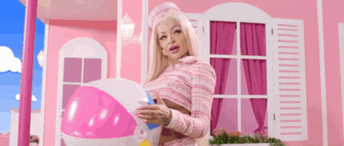 a woman dressed as a barbie doll holding a beach ball in front of a pink house