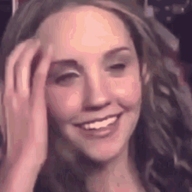 a close up of a woman 's face with her hand on her forehead and smiling .