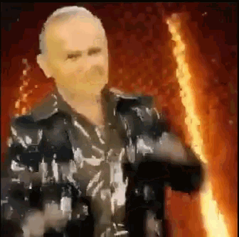 a man in a black jacket is holding a torch in front of a fire .