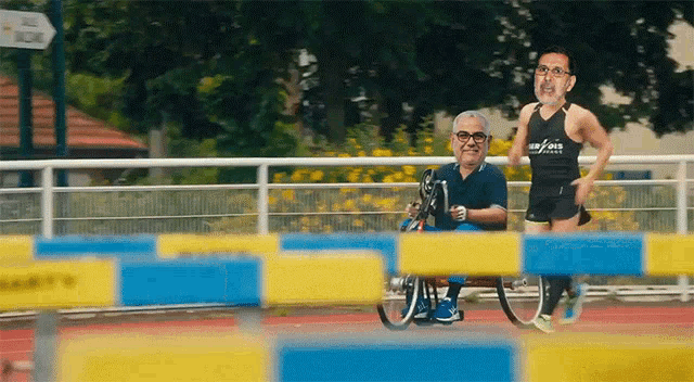 a man in a wheelchair is being pushed by a man in a black tank top that says u.s. forces