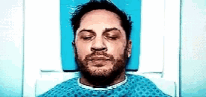 a man is laying in a hospital bed with his eyes closed and a beard .