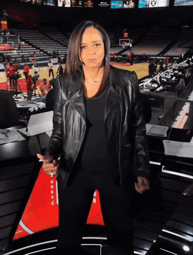 a woman in a leather jacket stands in front of an empty basketball court