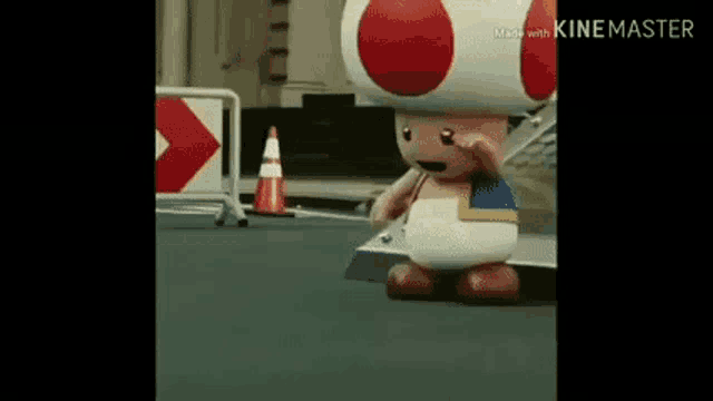 a toad mascot is standing on a sidewalk next to a traffic cone .